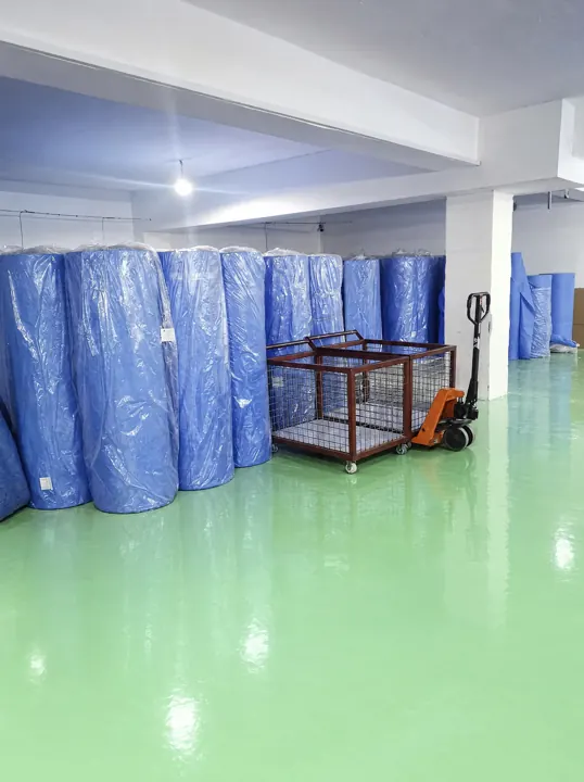 Warehouse area with our SMS fabric rolls, pallet jack and wire cage trolley | Lager – unsere SMS-Vliesrollen und Hubwagen | Magazzino – i nostri rotoli di tessuto SMS e transpallet